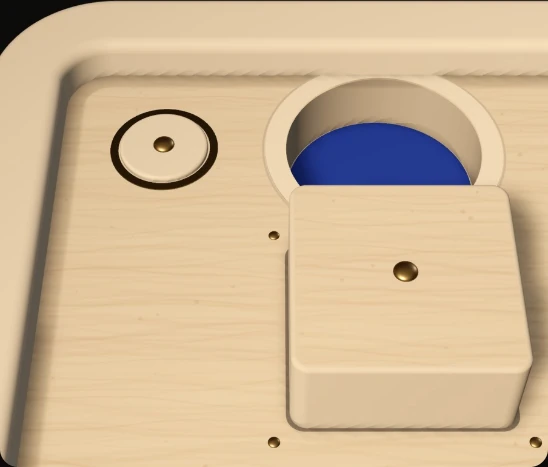 A square of the beech floor raised on its own four sides beside a hole, with a brass button ring nearby